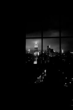 black and white photograph of city skyline from window at night time, looking out on skyscrapers