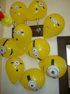 the balloons have been made to look like minion's faces and are hanging on the wall