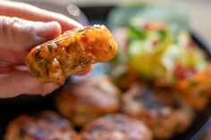 a hand holding a piece of food in front of a plate of vegetables and meat patties