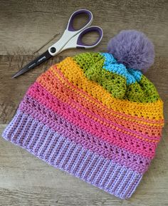 a crocheted hat with a pom - pom on top and scissors next to it