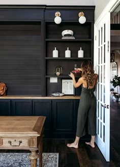 a woman standing in front of a kitchen counter with an open bookcase on the wall