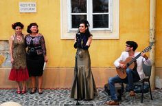 three women and one man are standing in front of a yellow building with a guitar