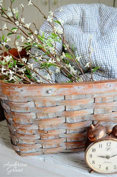 an old clock sitting next to a basket filled with flowers and other things in it