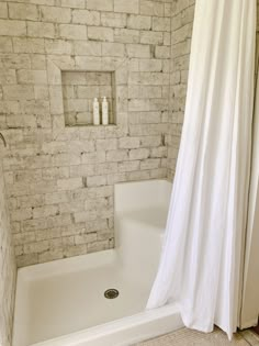 a white shower curtain in a bathroom next to a bathtub and toilet with a brick wall behind it