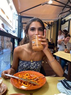 a woman sitting at a table with a plate of food in front of her and holding a coffee mug