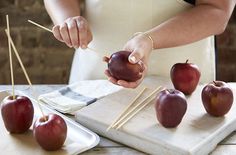 a person holding an apple on a stick in front of some apples and another one with toothpicks