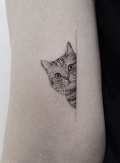 a small cat tattoo on the side of a woman's thigh, with an image of a cat peeking out from behind it