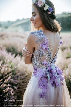 a woman in a dress with flowers on her head standing in a field full of wildflowers