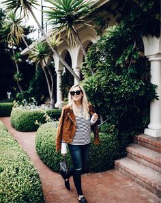 a woman standing in front of some bushes wearing sunglasses and a jacket with stripes on it