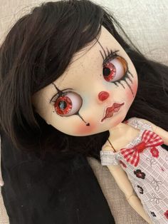 a doll with black hair and red eyes laying on a white surface next to a pillow