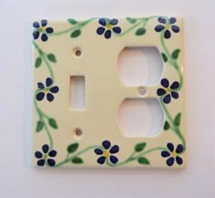 a white and blue flowered light switch cover with green leaves on it's sides