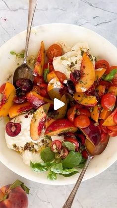 a white bowl filled with fruit and cheese on top of a marble table next to two spoons