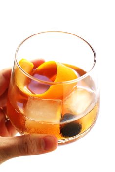 a hand holding a wine glass filled with liquid and sliced oranges on ice cubes