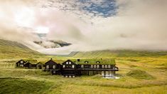 an aerial view of a house in the middle of a green field with mountains behind it