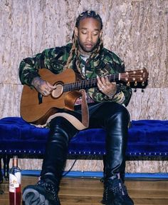 a man with dreadlocks sitting on a blue couch playing an ukulele