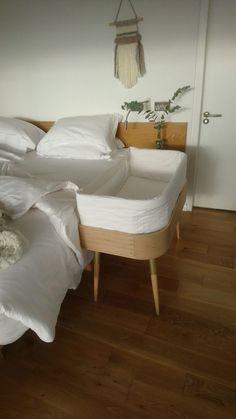 an unmade bed sitting on top of a wooden floor next to a white wall