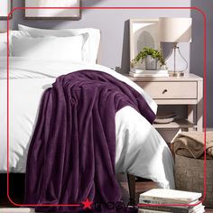 a bed with white sheets and purple blanket on top of it next to a nightstand