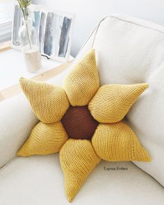 a yellow knitted star pillow sitting on a white couch next to a vase with flowers