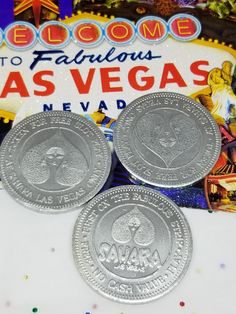 three silver coins sitting on top of a table next to a neon sign and confetti