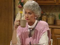 an older woman sitting at a table drinking from a cup