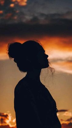 the silhouette of a woman with her hair blowing in the wind, against a sunset sky