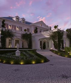 a large white house with lots of windows and plants on the front lawn at dusk