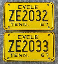 two yellow license plates with black numbers are on a piece of gray fabric, one has the words cycle ze03 and the other says ten