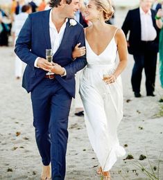 a man and woman are walking on the beach with drinks in their hands as people walk behind them