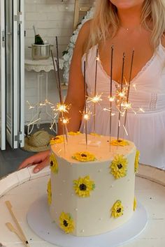 a woman standing in front of a cake with sparklers on it and sunflowers