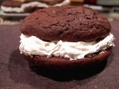 a chocolate cookie sandwich with whipped cream on it sitting on a brown cloth next to other cookies