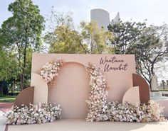 a sign that has flowers on it in front of trees and bushes with buildings in the background