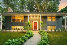 a house that is in the grass with trees and bushes on either side of it