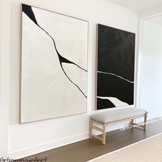 two black and white paintings hang on the wall next to a bench in an empty room