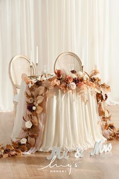 a table with chairs and flowers on it for a wedding reception in front of a white curtain