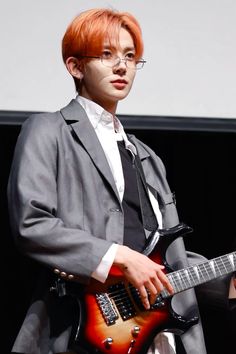 a man with red hair and glasses playing an electric guitar