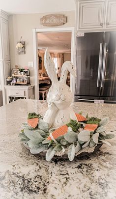 a white rabbit statue sitting on top of a kitchen counter next to a wreath filled with carrots