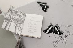 two butterflies are on the table next to an open book with a tassel hanging from it