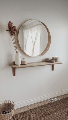 a round mirror on a wall above a shelf with vases and other items in front of it