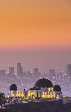 the city lights shine brightly in the distance as seen from atop a hill at dusk