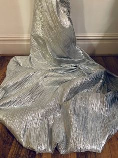 a silver dress sitting on top of a wooden floor in front of a white wall