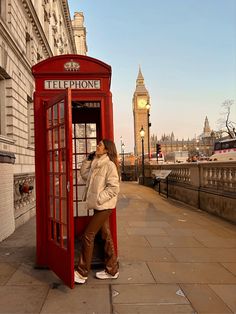 a woman standing next to a red phone booth