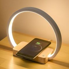 a cell phone sitting on top of a wooden table next to a charging dock with an led light