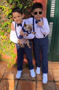 two young boys dressed in blue pants and white shirts, one holding a small dog