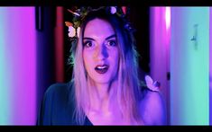 a woman with long blonde hair wearing a flower crown in front of purple and blue lights