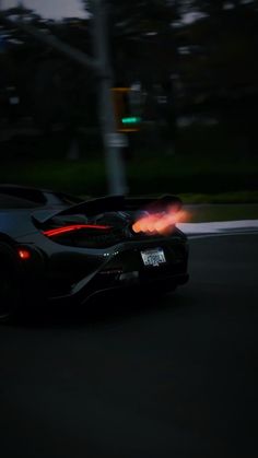 a black sports car driving down the road at night with red lights on it's headlights