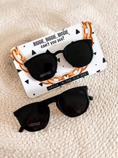 two pairs of black sunglasses sitting on top of a white sheet with an orange ribbon