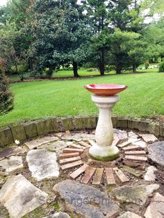 a bird bath sitting in the middle of a stone circle surrounded by grass and trees