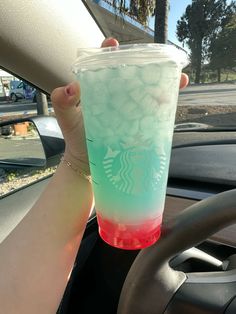 a person holding up a starbucks drink in their hand on the steering wheel of a car