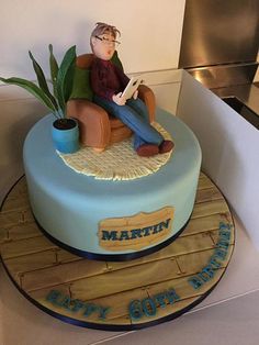 a birthday cake with a man sitting in a chair reading a book on top of it