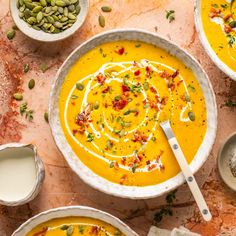 two bowls filled with carrot soup and topped with pistachio seeds next to spoons